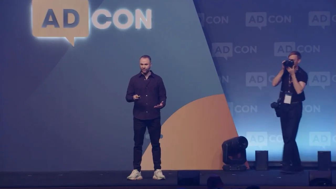 ผู้พูดบนเวที Adcon ยืนบรรยาย พร้อมโลโก้ AD CON และทีมงานกล้อง