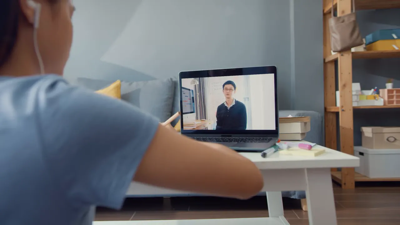 คนกำลังเรียนจากแล็ปท็อป ดูวิดีโอสอนบนหน้าจอ ขณะจดหรือทำงานที่โต๊ะ