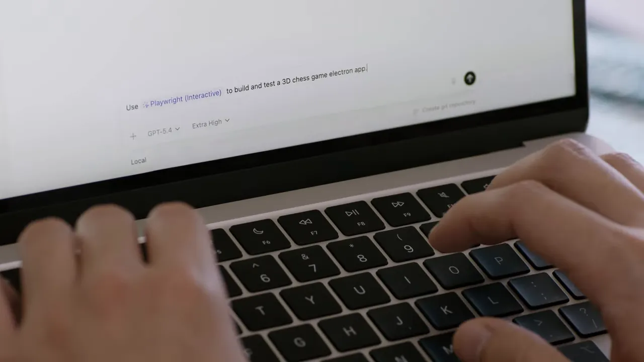 Laptop screen showing 'Use Playwright (Interactive) to build and test a 3D chess game' with hands on the keyboard